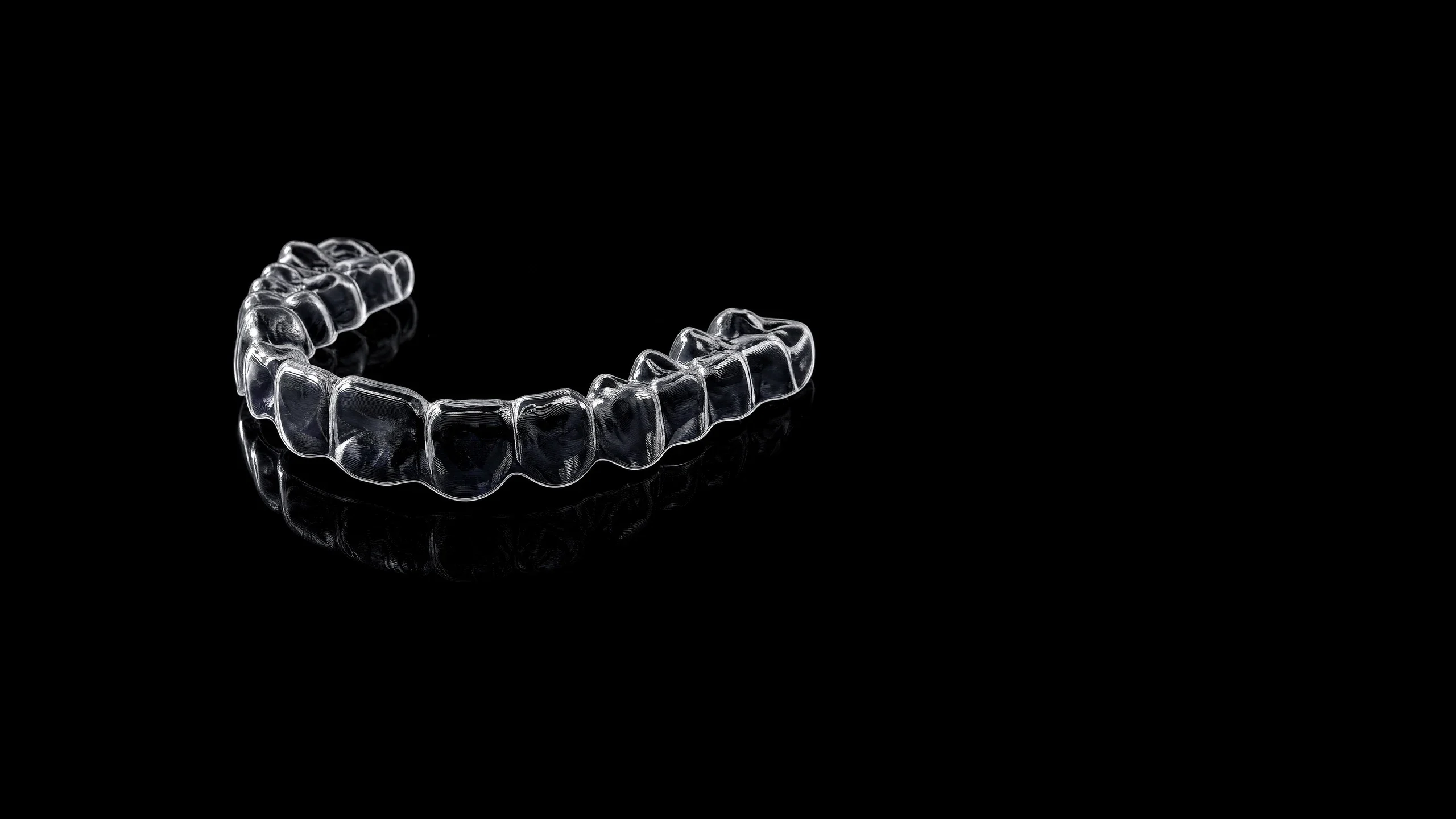A clear orthodontic aligner held between gloved fingers against black